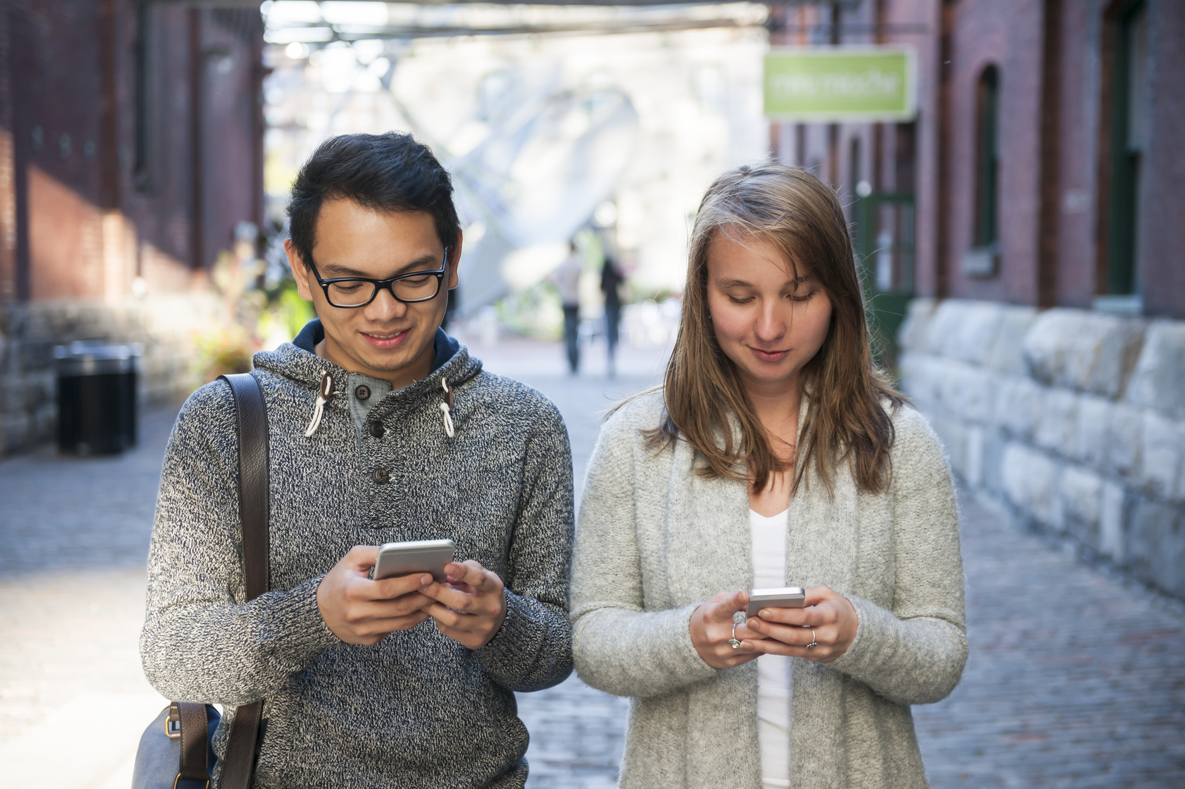 two people looking at their phones while walking along the street