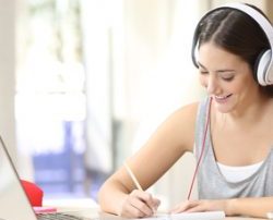 student wearing headphones while writing and working in front of a laptop