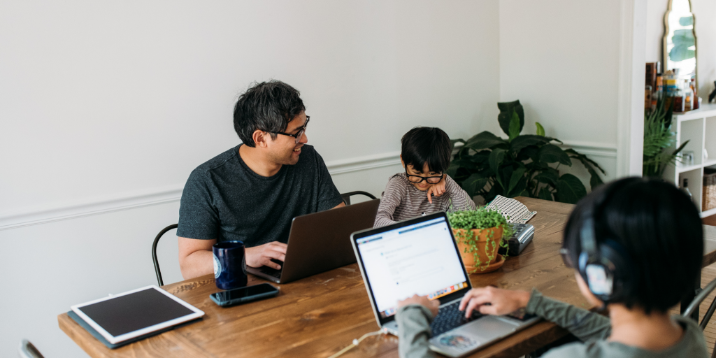 Adult sitting at table with two various-aged children with laptops